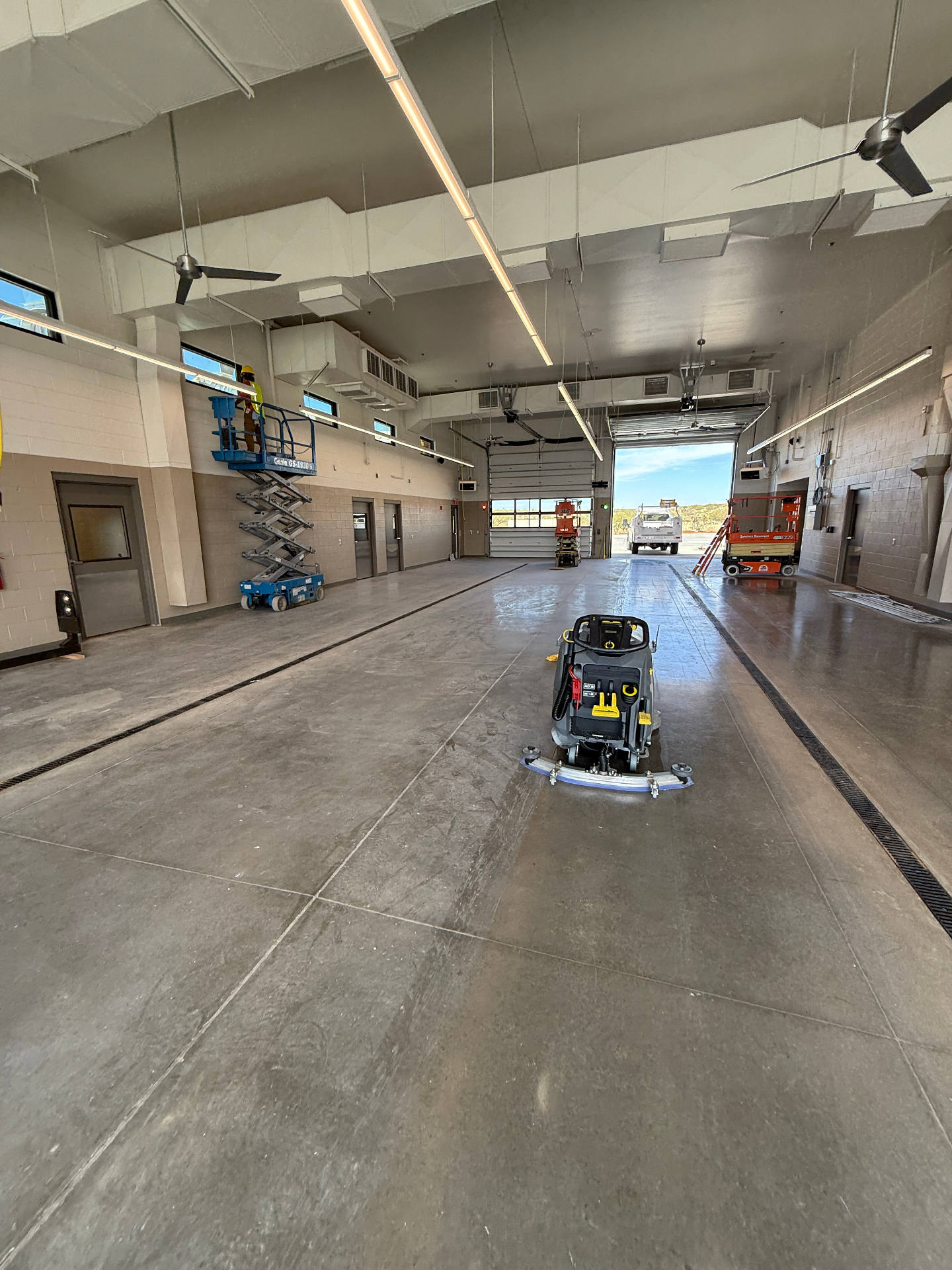 Ride-on floor scrubber polishing the concrete floor of a large apparatus bay